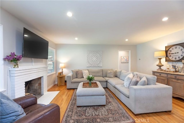 living area featuring recessed lighting, baseboards, a brick fireplace, and light wood-type flooring