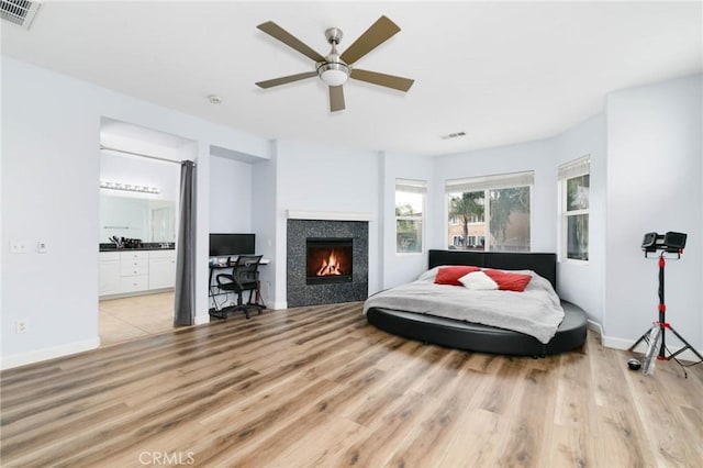 bedroom with baseboards, visible vents, a tiled fireplace, and wood finished floors