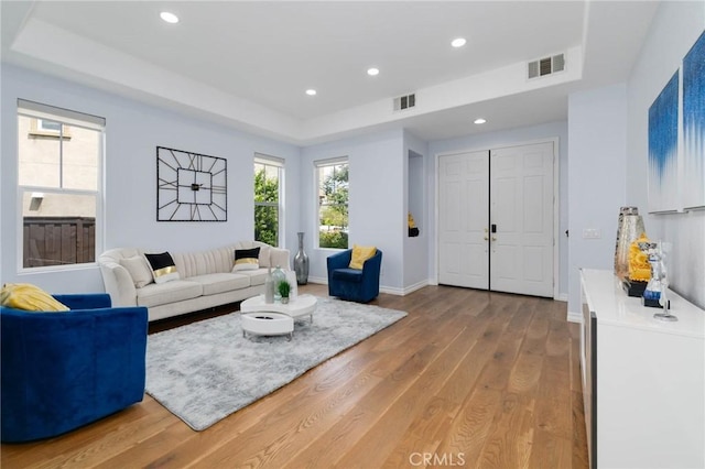 living room with recessed lighting, visible vents, wood finished floors, and a raised ceiling