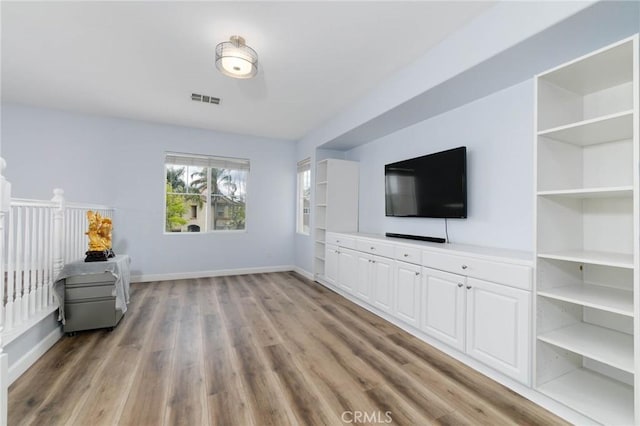unfurnished living room with baseboards, visible vents, and wood finished floors