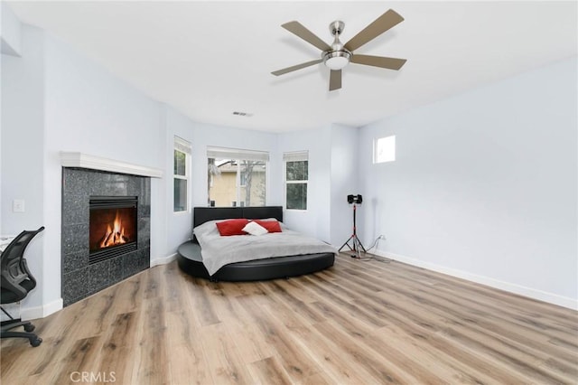 bedroom with a tiled fireplace, baseboards, and wood finished floors