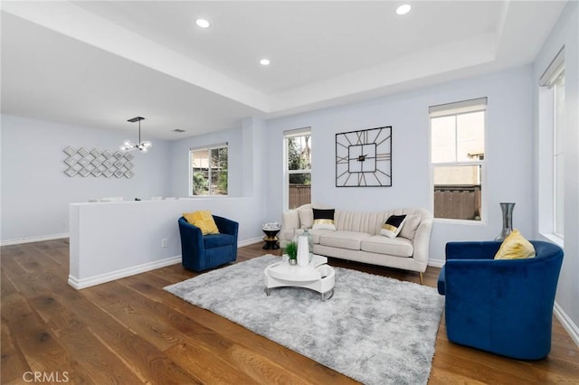 living room with baseboards, a chandelier, a raised ceiling, and dark wood-type flooring