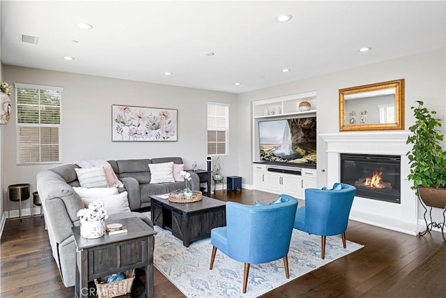 living area featuring wood-type flooring, visible vents, a glass covered fireplace, baseboards, and recessed lighting