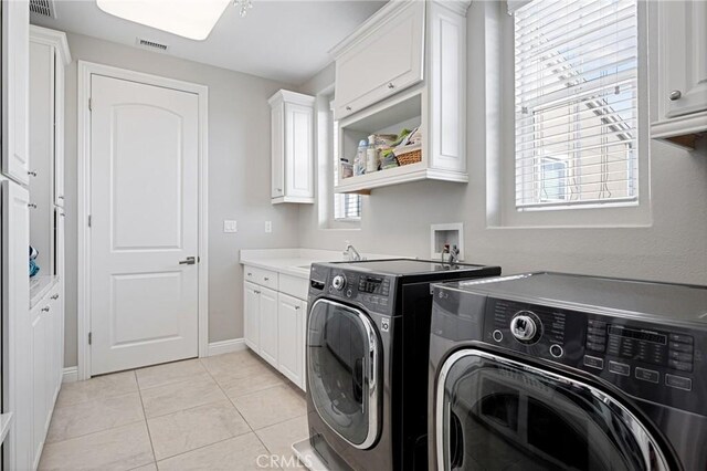 washroom with light tile patterned floors, washing machine and dryer, cabinet space, and visible vents