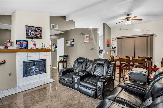 tiled living area with a tiled fireplace, ceiling fan, vaulted ceiling, and visible vents