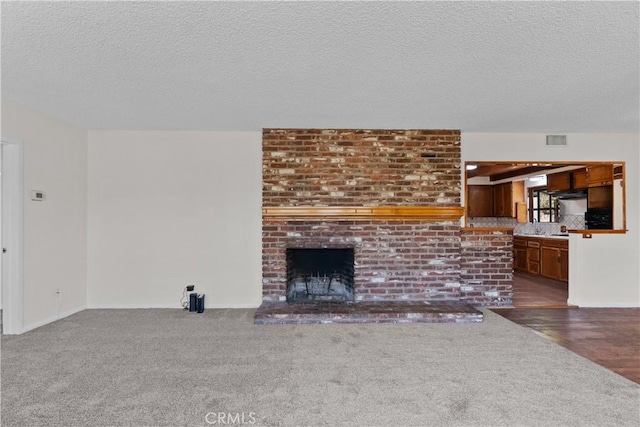 unfurnished living room featuring carpet floors, a brick fireplace, a textured ceiling, and visible vents