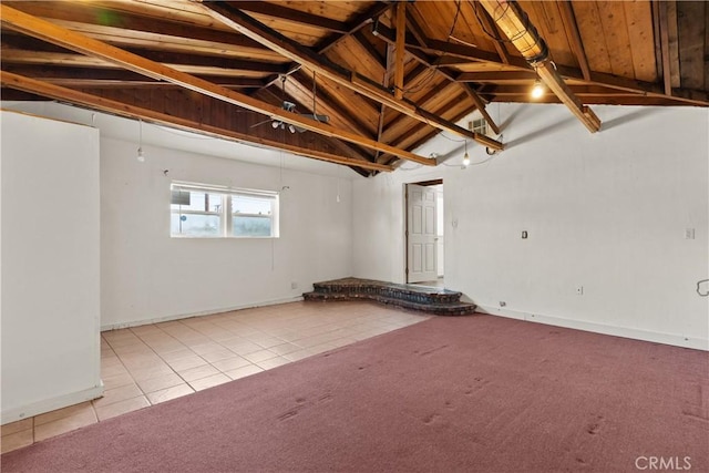 carpeted empty room with tile patterned floors, baseboards, and lofted ceiling