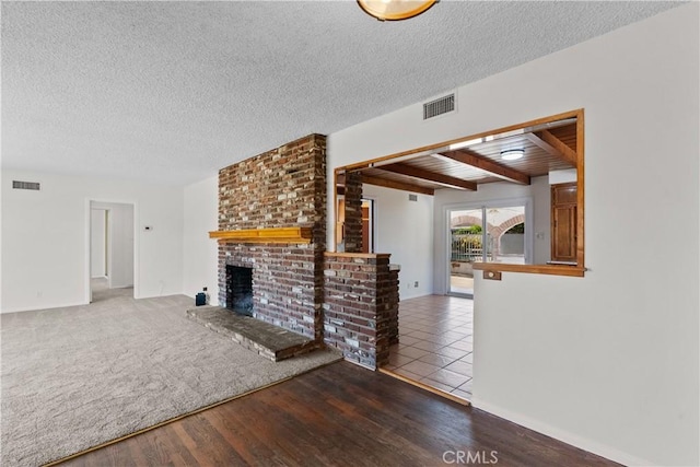 unfurnished living room featuring visible vents, a textured ceiling, a brick fireplace, and wood finished floors