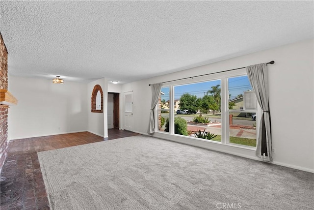 unfurnished living room with a textured ceiling, baseboards, and carpet