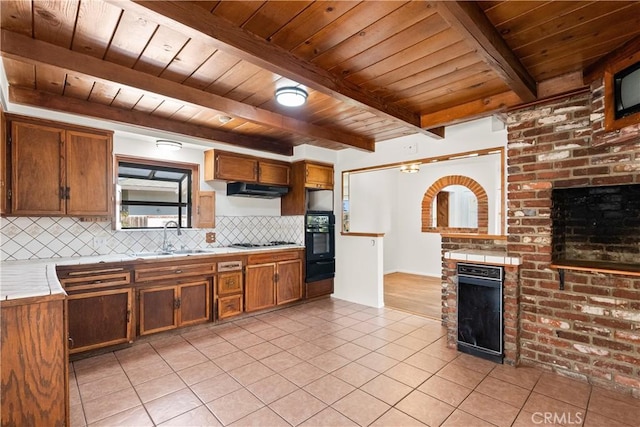 kitchen featuring beamed ceiling, wooden ceiling, a sink, and a fireplace