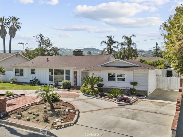 ranch-style home with roof with shingles, fence, a chimney, and concrete driveway