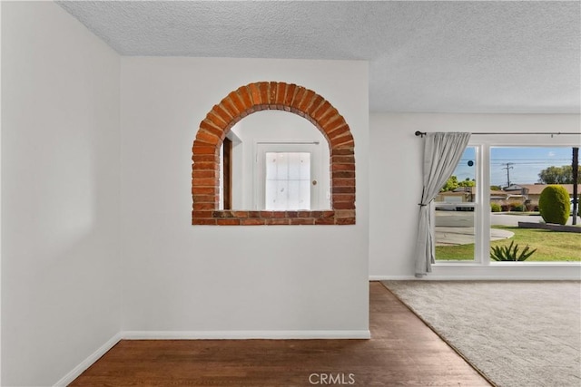 interior space with a textured ceiling, baseboards, and wood finished floors