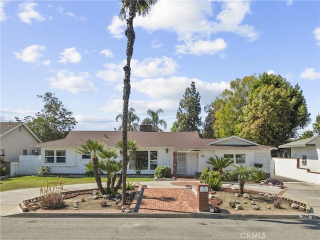 ranch-style home with roof with shingles, fence, driveway, and a chimney