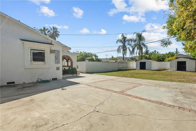 view of patio / terrace with a storage shed, fence, an outbuilding, and driveway