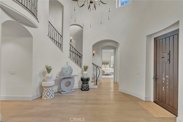 foyer with baseboards, arched walkways, wood finished floors, and a towering ceiling