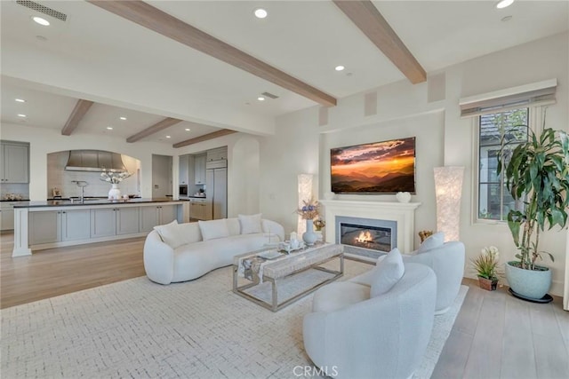 living area with beamed ceiling, visible vents, and light wood-style floors
