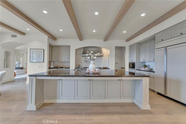 kitchen with arched walkways, a sink, paneled refrigerator, and gray cabinetry