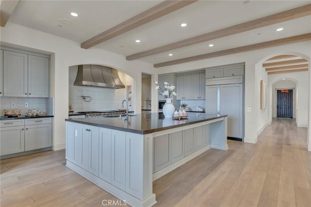 kitchen with gray cabinetry, dark countertops, arched walkways, and wall chimney exhaust hood