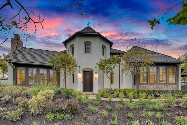 back of property at dusk with a chimney and stucco siding