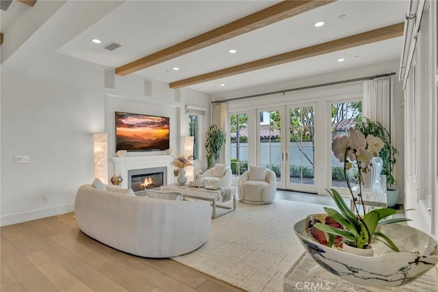 living area with french doors, beam ceiling, wood finished floors, baseboards, and a glass covered fireplace
