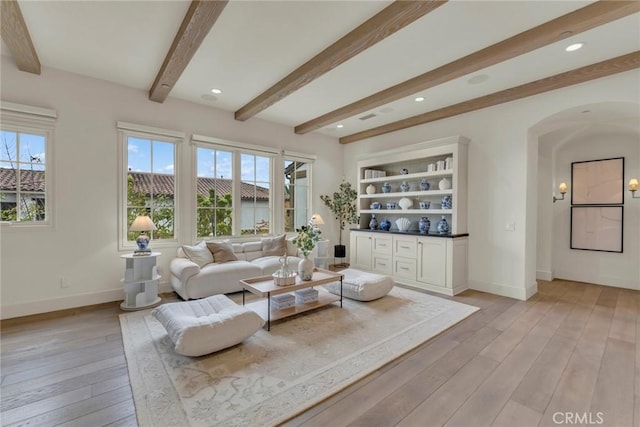 living room with baseboards, light wood-style floors, a healthy amount of sunlight, and beamed ceiling