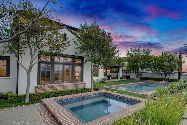 exterior space with fence, an in ground hot tub, stucco siding, and brick siding