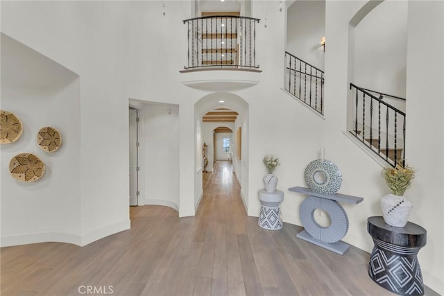 foyer with arched walkways, a towering ceiling, wood finished floors, and stairway