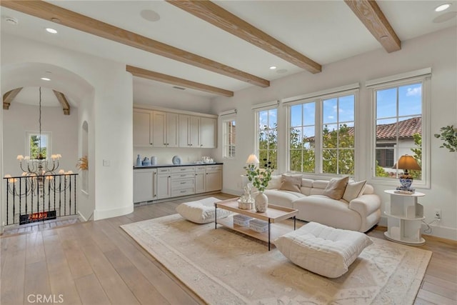 living room with light wood-style floors, baseboards, beam ceiling, and a chandelier
