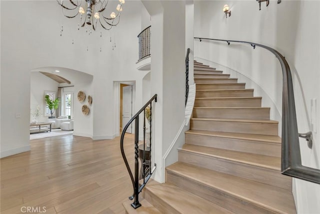 staircase with arched walkways, a high ceiling, wood finished floors, and a chandelier