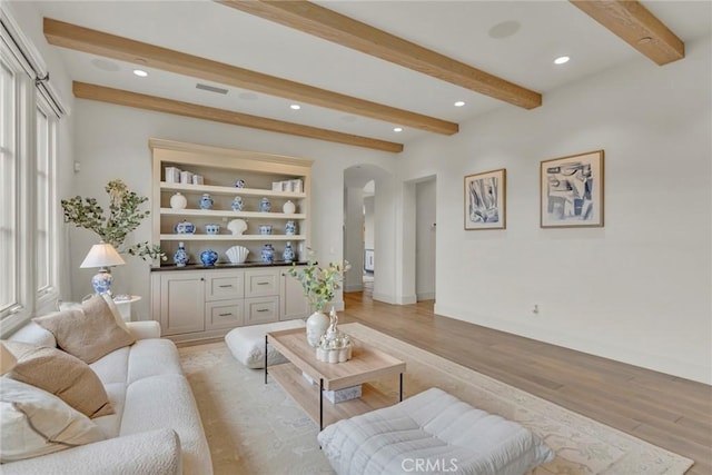 living area featuring arched walkways, beam ceiling, baseboards, light wood finished floors, and recessed lighting