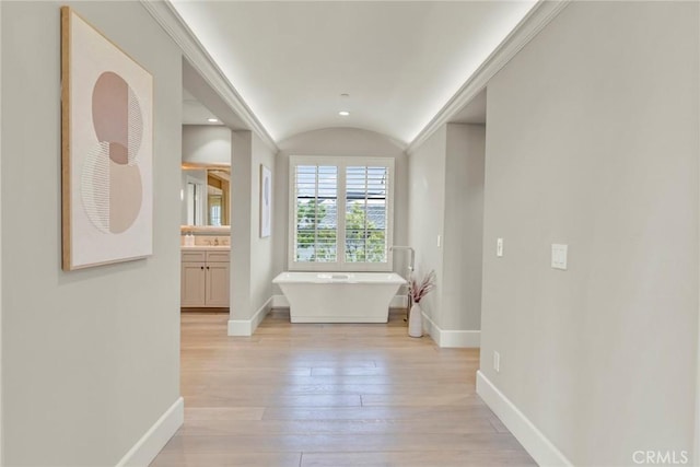 corridor featuring baseboards, lofted ceiling, and light wood finished floors