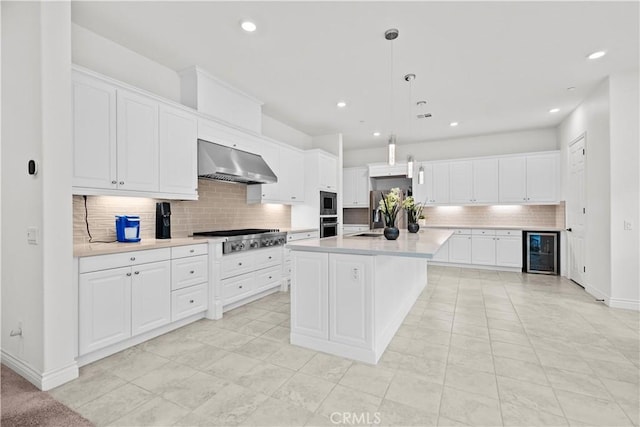 kitchen featuring decorative backsplash, wine cooler, light countertops, under cabinet range hood, and appliances with stainless steel finishes