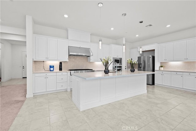 kitchen featuring light countertops, stainless steel appliances, white cabinetry, tasteful backsplash, and under cabinet range hood