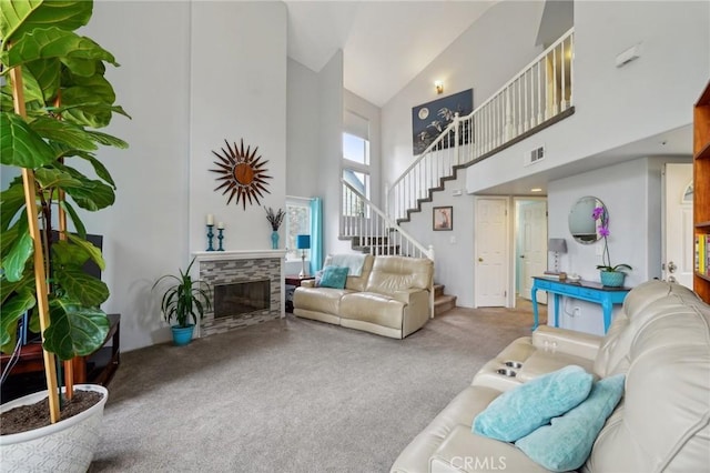 carpeted living area with visible vents, stairs, a stone fireplace, and high vaulted ceiling