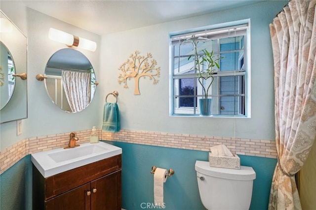 full bath with tile walls, vanity, toilet, and a wealth of natural light