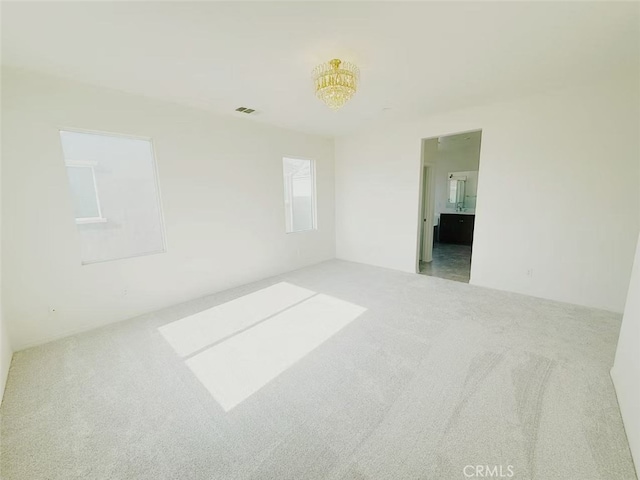 carpeted empty room featuring a chandelier and visible vents