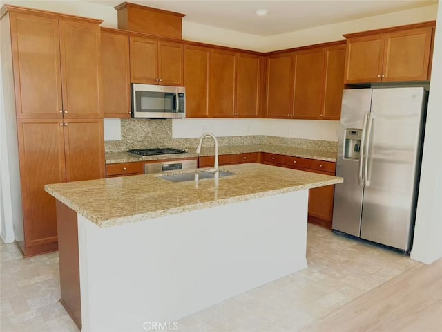 kitchen featuring a kitchen island with sink, light stone countertops, tasteful backsplash, a sink, and appliances with stainless steel finishes