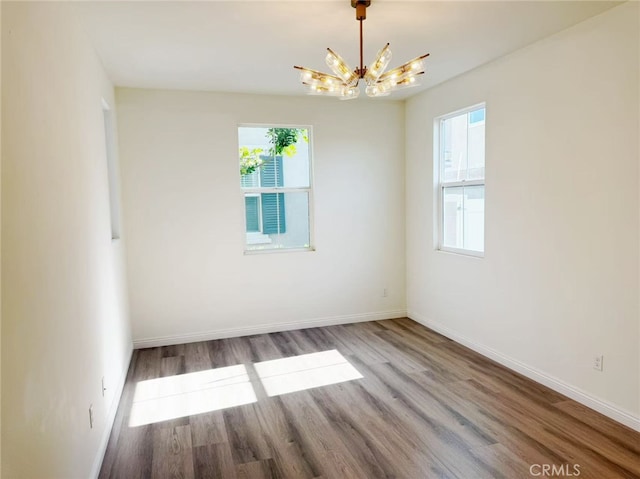 empty room with baseboards, a chandelier, and wood finished floors