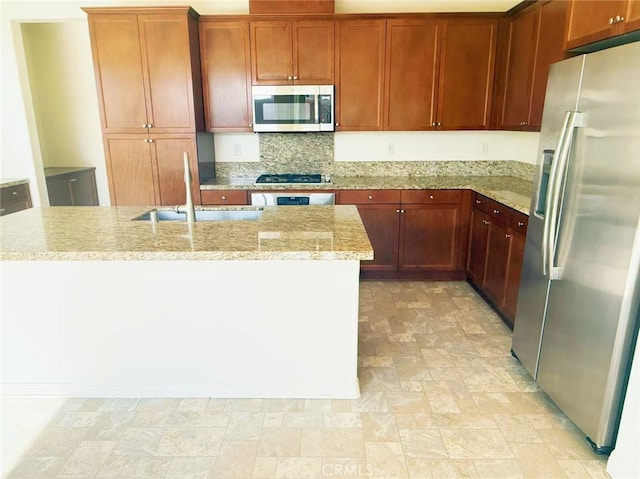 kitchen with decorative backsplash, stone finish floor, light stone counters, a sink, and appliances with stainless steel finishes