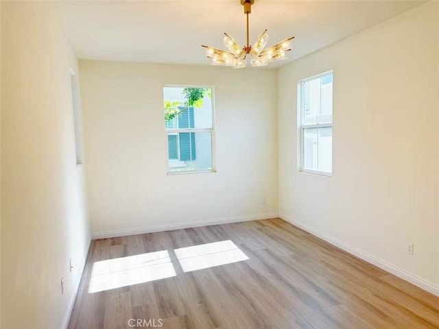 empty room featuring an inviting chandelier, baseboards, and light wood-type flooring