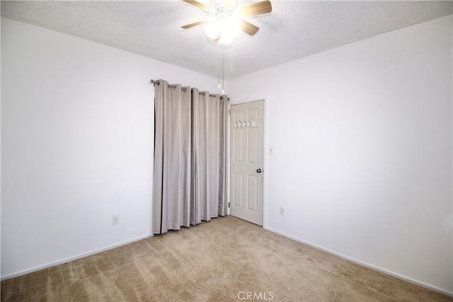 empty room featuring ceiling fan, light carpet, and baseboards