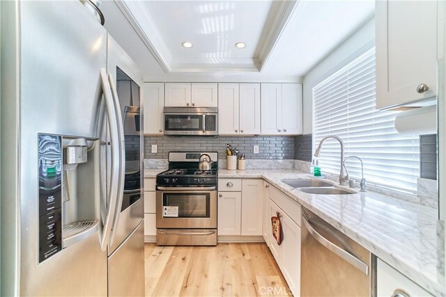 kitchen with decorative backsplash, appliances with stainless steel finishes, white cabinetry, a sink, and light wood-style flooring