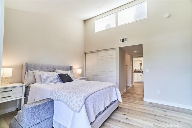 bedroom with visible vents, a closet, a towering ceiling, baseboards, and light wood-style flooring
