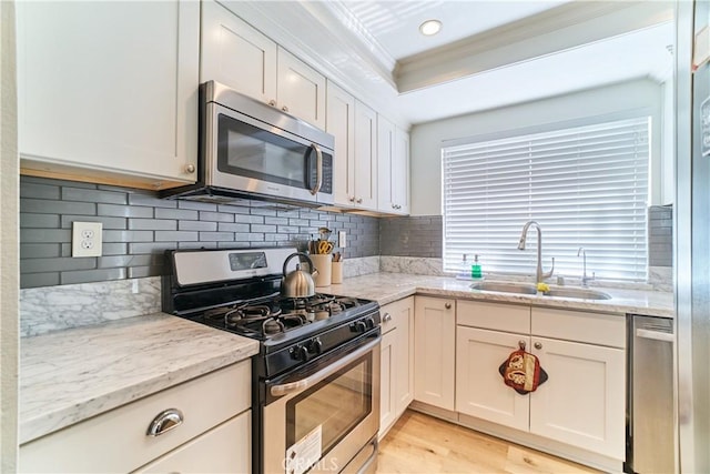 kitchen featuring crown molding, a sink, light wood-style flooring, stainless steel appliances, and decorative backsplash