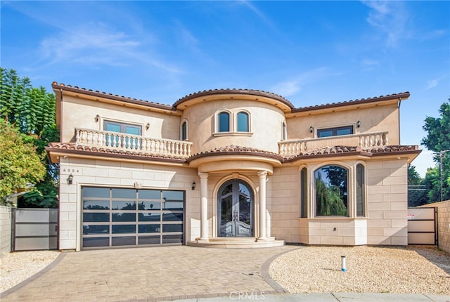 mediterranean / spanish house with fence, a balcony, decorative driveway, stucco siding, and french doors