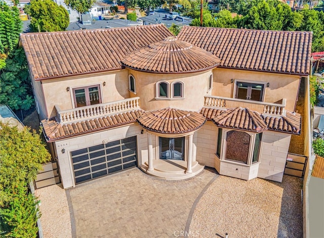 mediterranean / spanish house featuring a balcony, decorative driveway, french doors, a tiled roof, and an attached garage