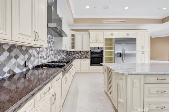 kitchen featuring marble finish floor, wall chimney exhaust hood, tasteful backsplash, dark stone countertops, and appliances with stainless steel finishes