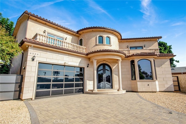 mediterranean / spanish-style home featuring a garage, stucco siding, decorative driveway, a balcony, and french doors