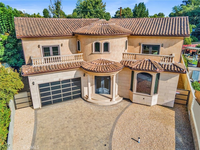 mediterranean / spanish-style house with french doors, a garage, decorative driveway, fence, and a balcony