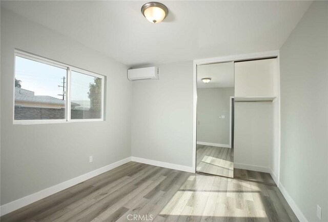 5459 Carlin St, Los Angeles, CA 90016 - unfurnished bedroom with baseboards, a closet, a wall mounted air conditioner, and wood finished floors